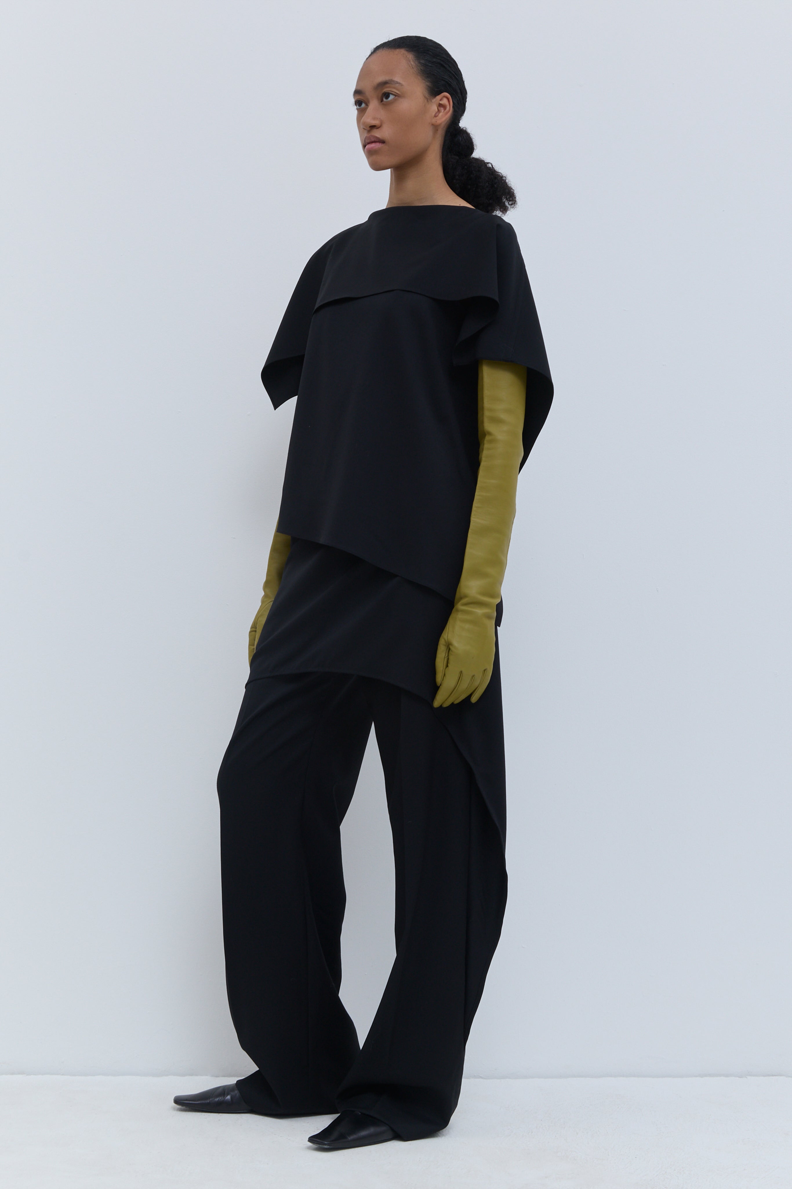 Front view of the black wool sleeveless top with an asymmetric layered panel.