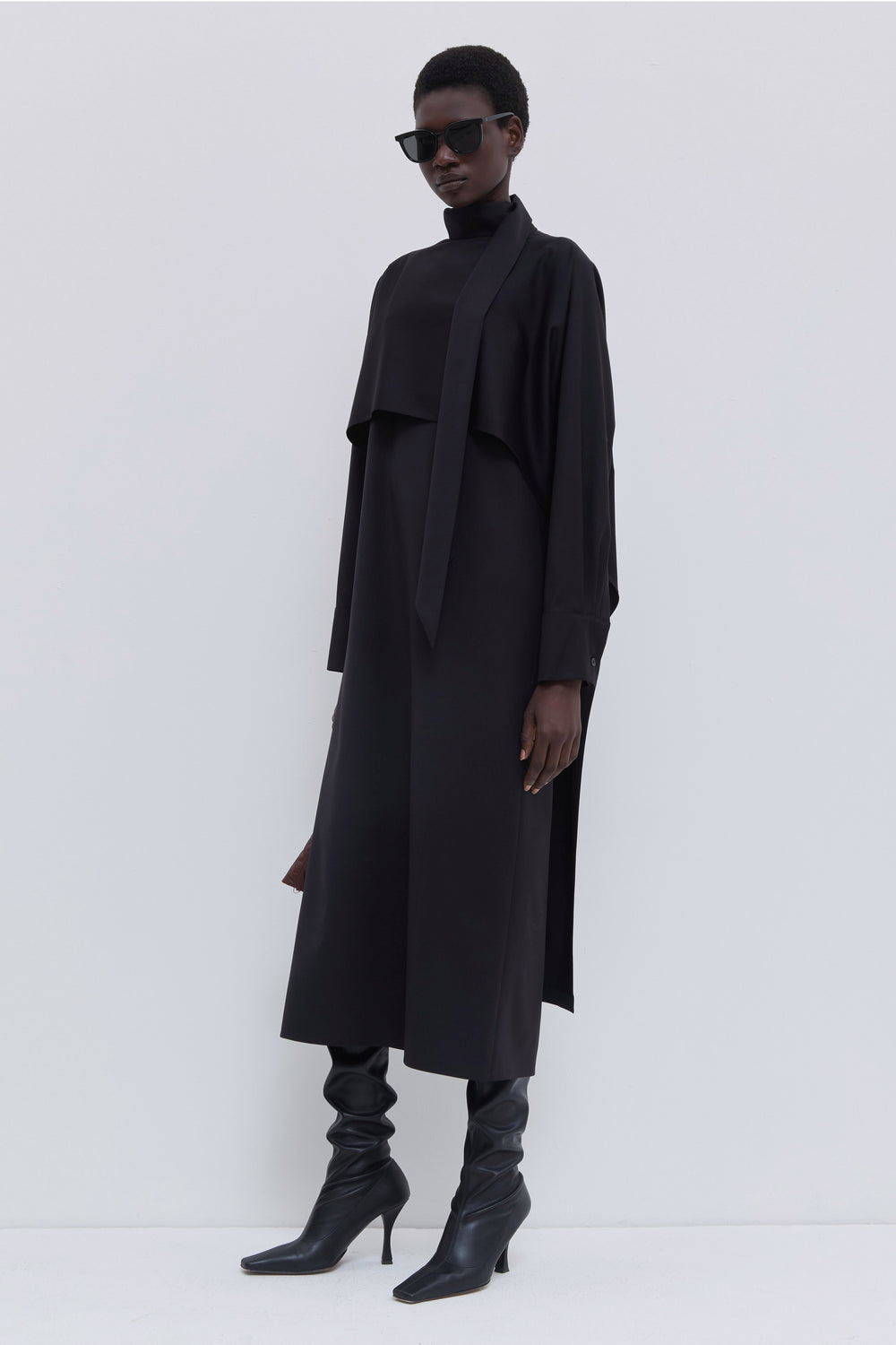 Front view of a black long-sleeve virgin wool dress with draped scarf detail.