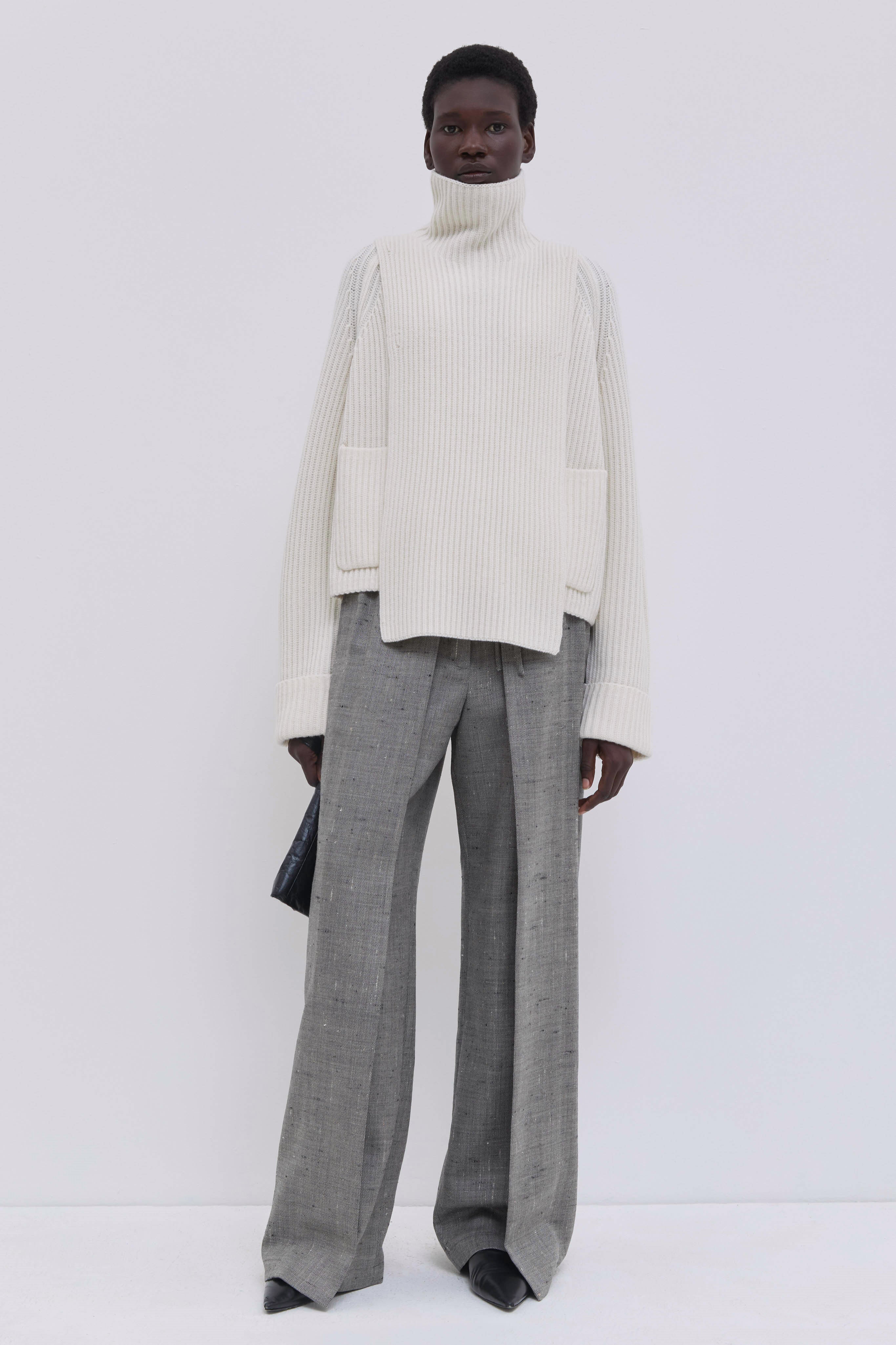 Cream ribbed merino wool and cashmere knit bib with oversized turtleneck, layered over wide-leg tailored trousers.
