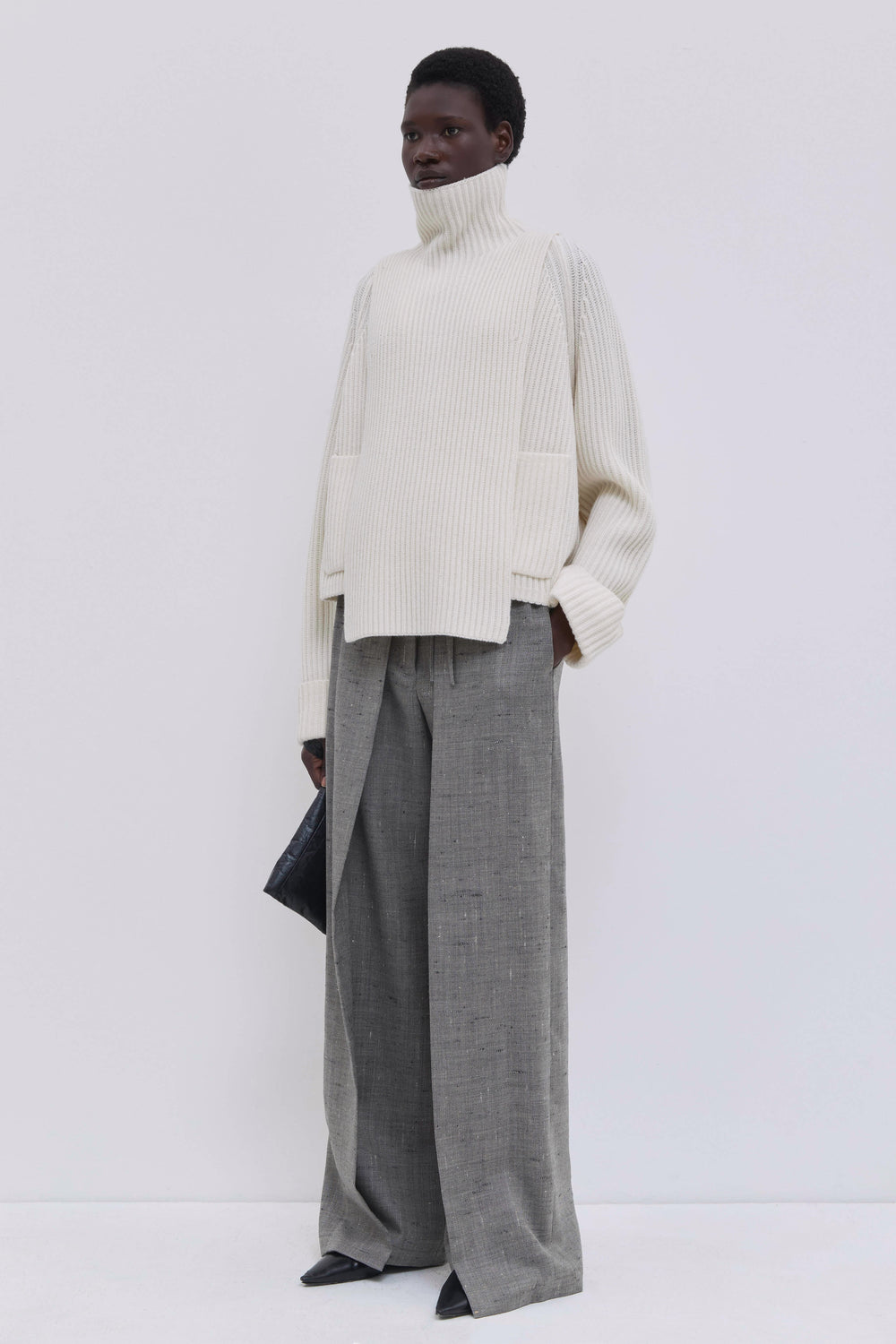 Cream ribbed merino wool and cashmere knit bib with high ribbed turtleneck, styled with tailored grey wool trousers.