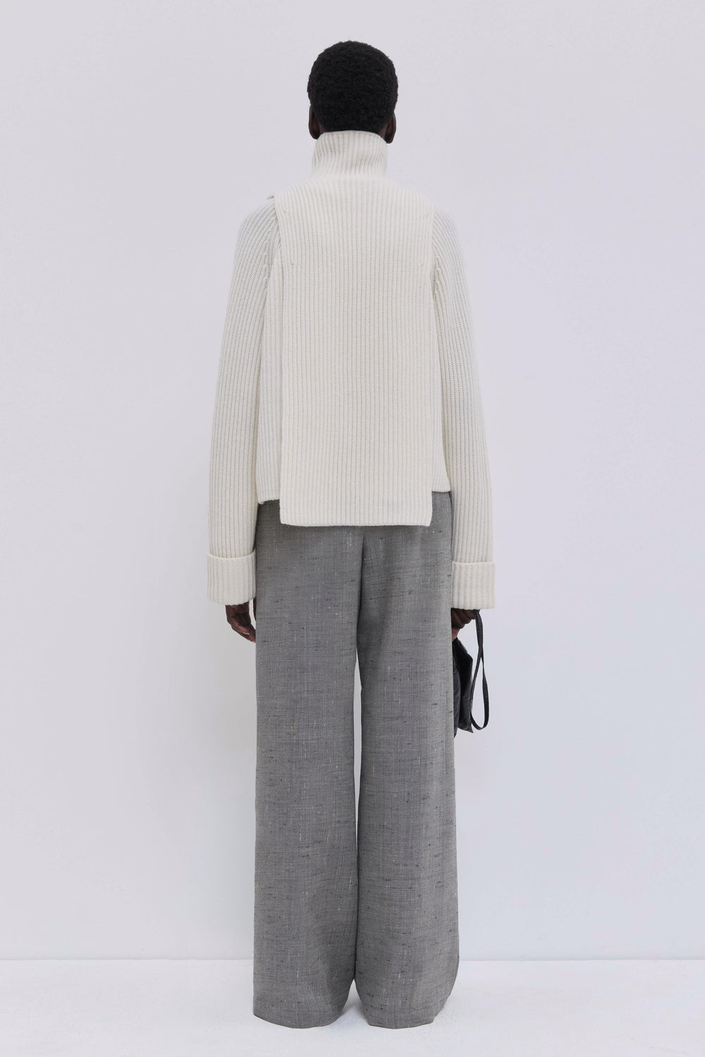 Back view of cream ribbed merino wool and cashmere knit bib with elongated silhouette and oversized turtleneck.