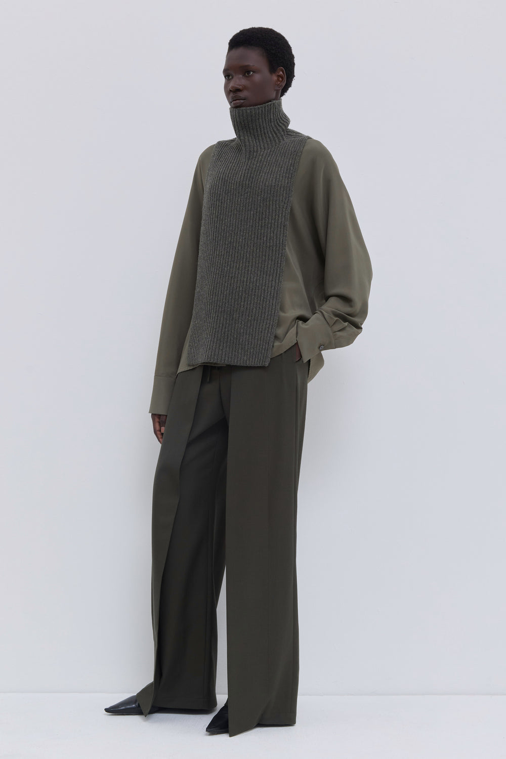 Forest melange ribbed merino wool and cashmere knit bib with high ribbed turtleneck layered over an olive blouse.
