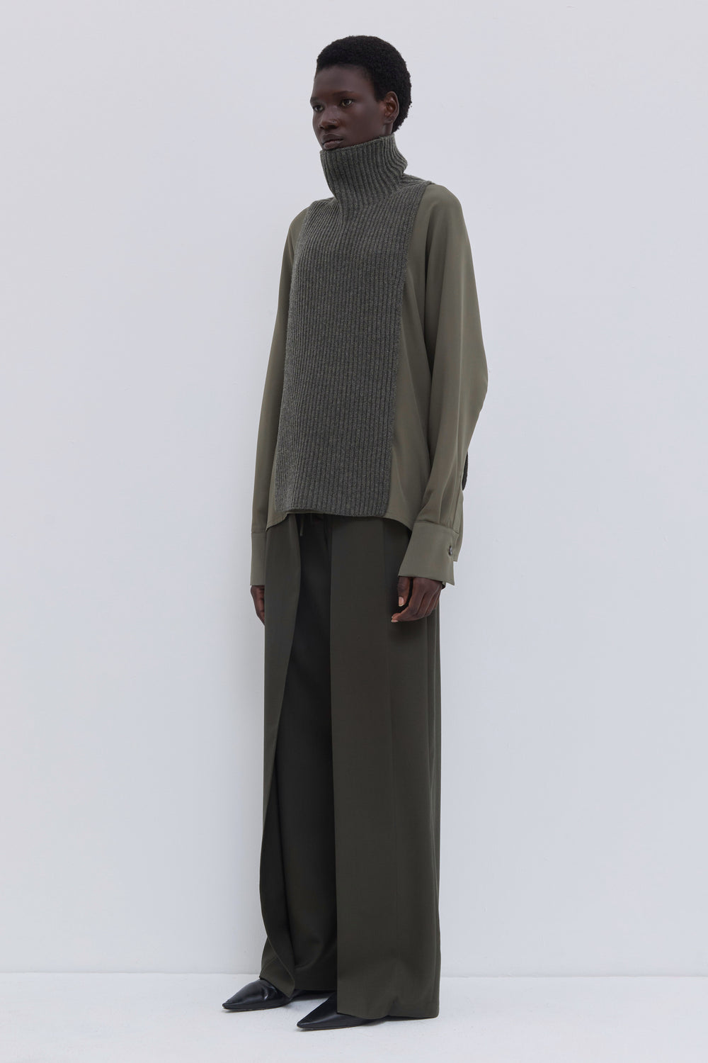 Forest melange ribbed merino wool and cashmere knit bib with oversized turtleneck styled with an olive blouse and wide-leg trousers.