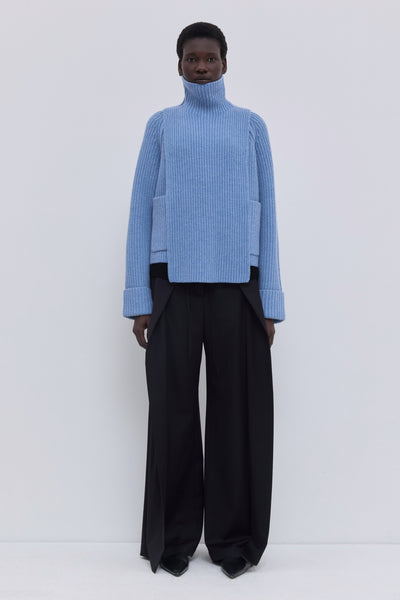 Mirage blue ribbed merino wool and cashmere knit bib with oversized turtleneck, layered under a cropped blazer with tailored wide-leg trousers.