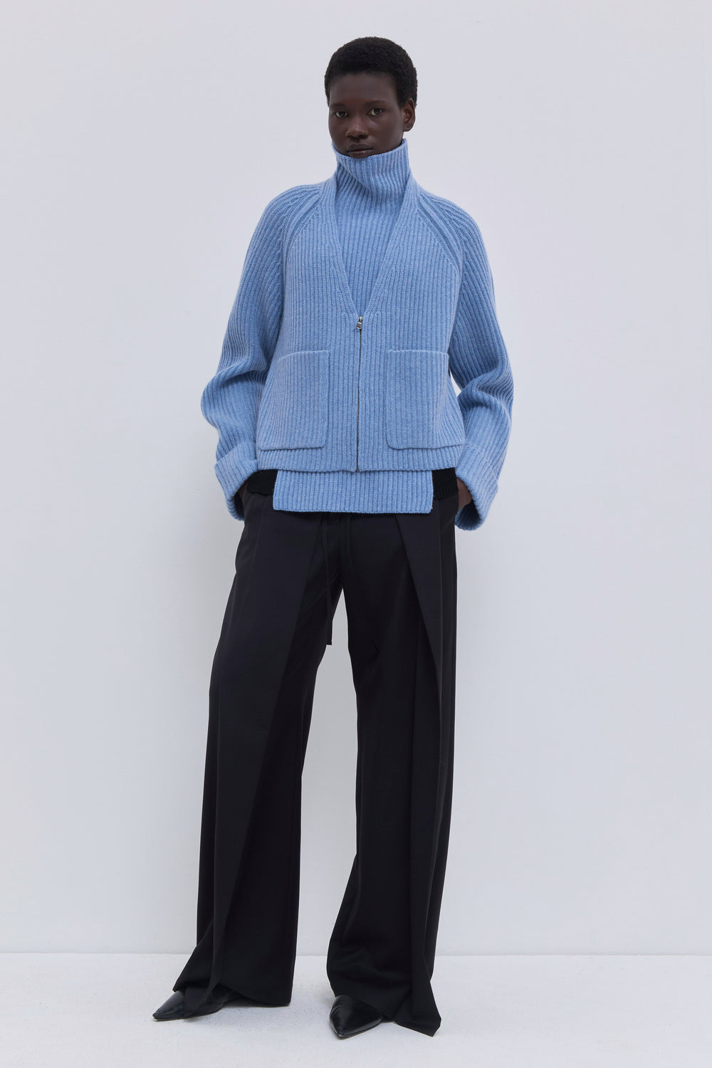 Mirage blue ribbed merino wool and cashmere knit bib with oversized turtleneck styled with a cropped blazer and tailored trousers.