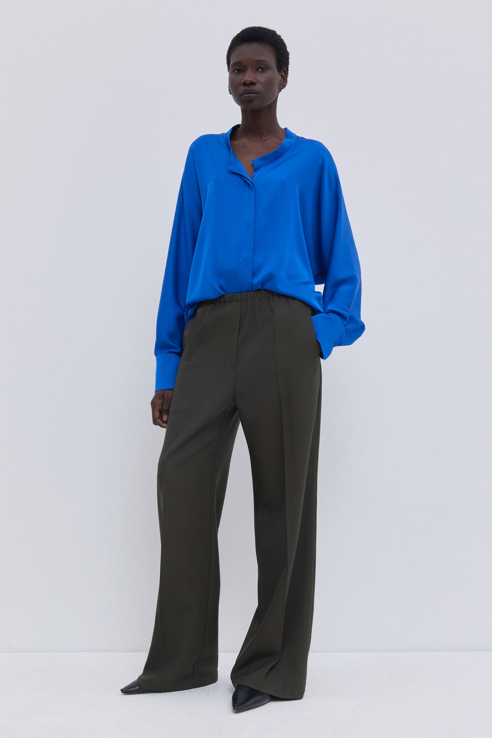Front view of low-waisted dark forest wool trousers with rounded pockets.