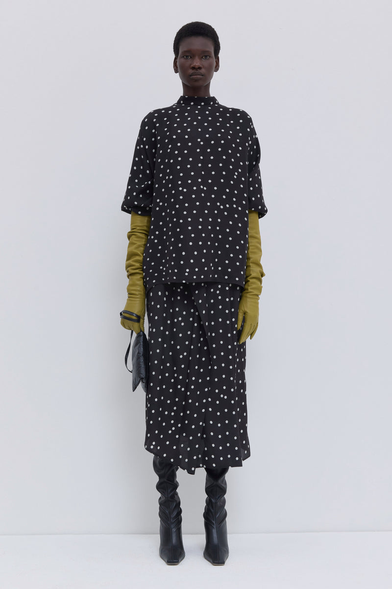 Model wearing a black lady bug print draped skirt with elastic waistband and asymmetric hem by Christian Wijnants.